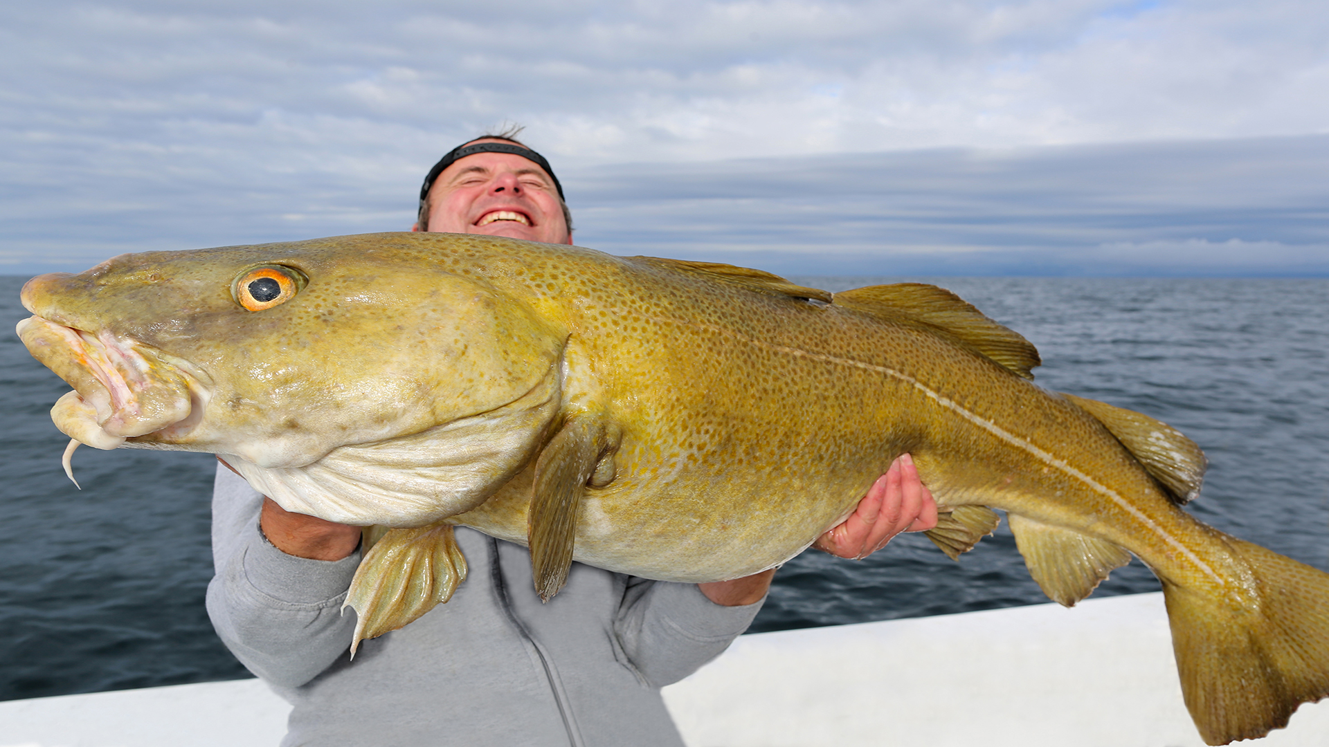 På biletet ser vi ein man som held ein kjempestor fisk på ein båt